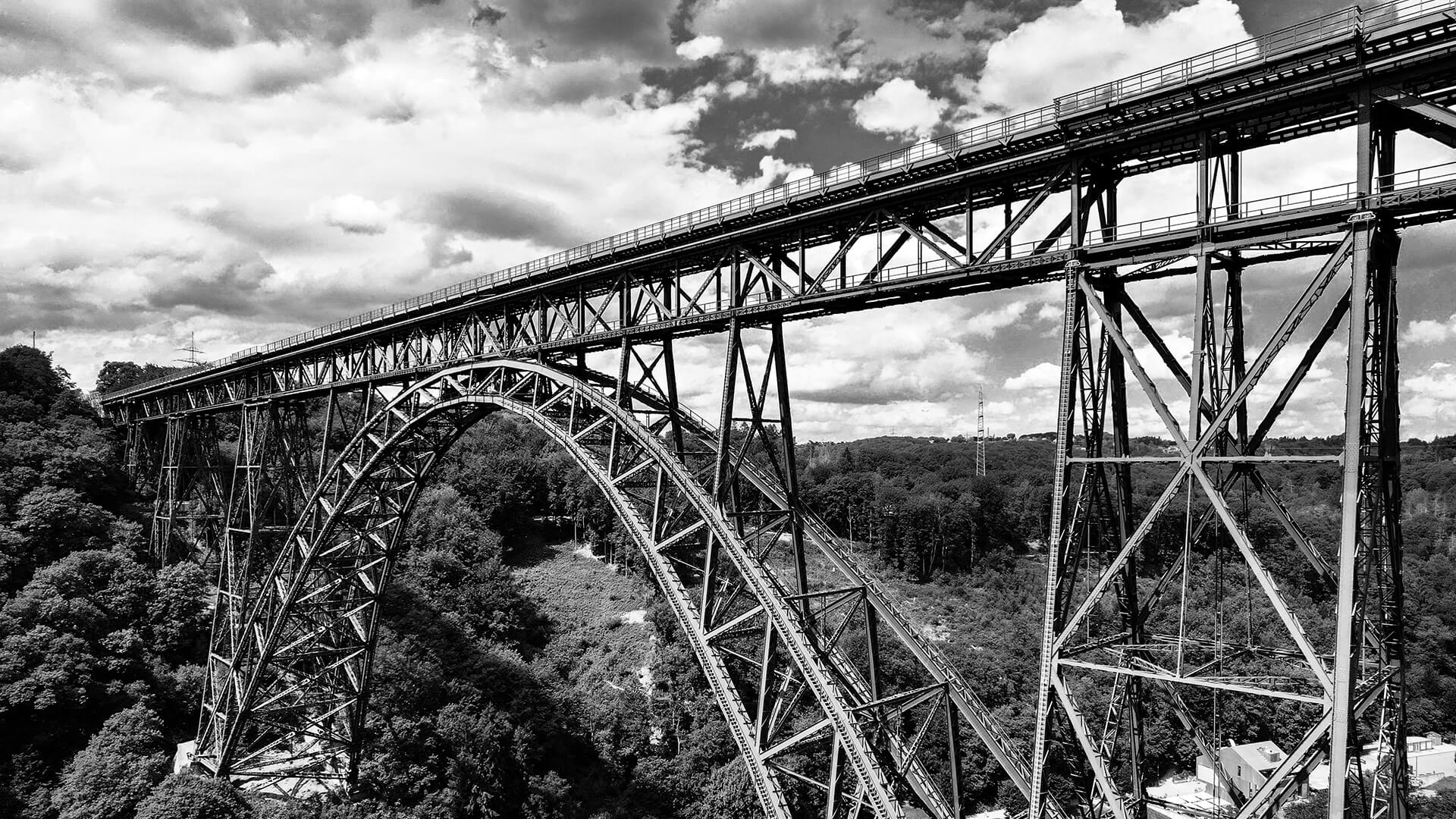 Die Müngstener Brücke in Solingen als imposante Schwarz-Weiß-Fotografie, Blick auf die Stahlkonstruktion und das bewaldete Tal